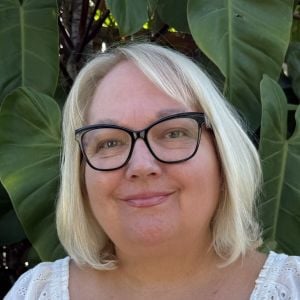 Smiling woman with glasses outdoors near green leaves